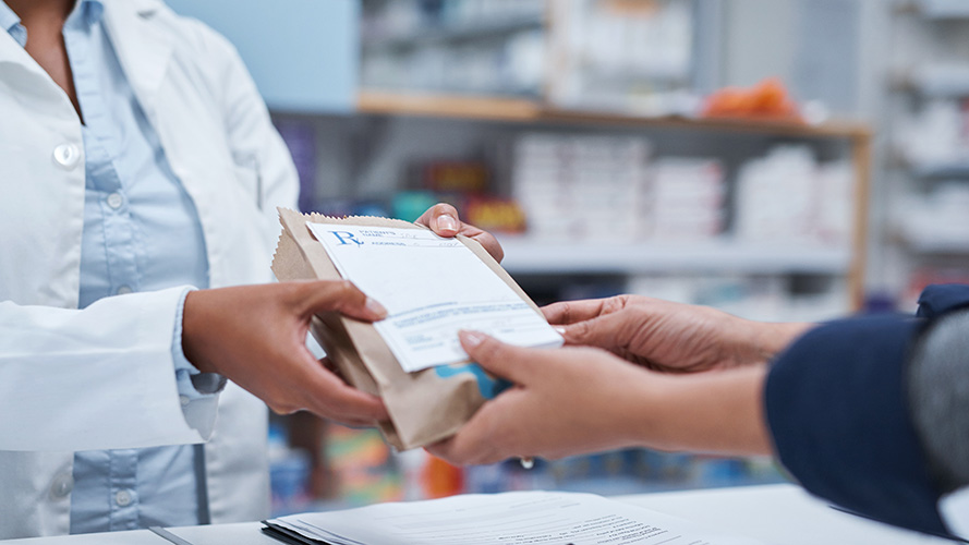 A prescription bag being passed from the hands of a pharmacist to the hands of a customer