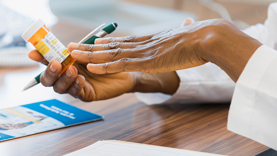 Les mains d'un pharmacien tenant un flacon de médicaments et un stylo vert